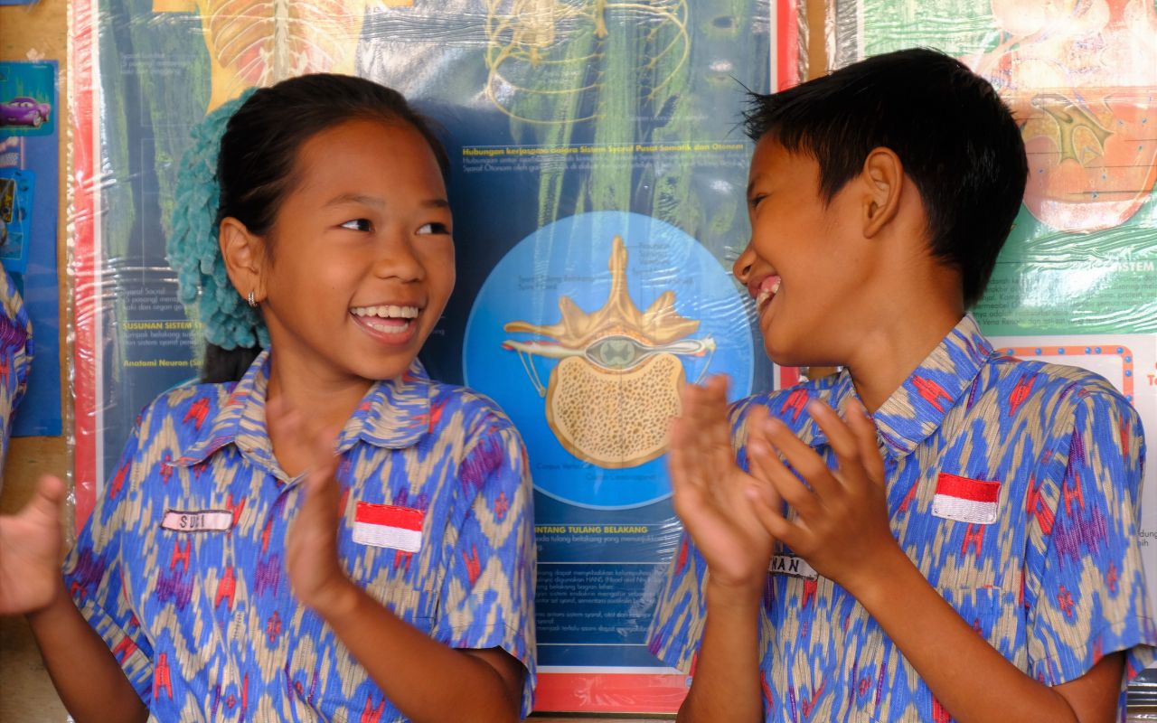 Lachendes indonesisches Mädchen und Junge in farbenfroh gemusterten Schuluniformen